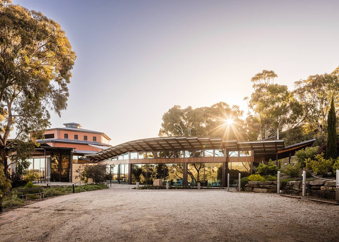 Exterior view of the Ukaria Cultural Centre on a blue sky morning, the sun poking through the trees