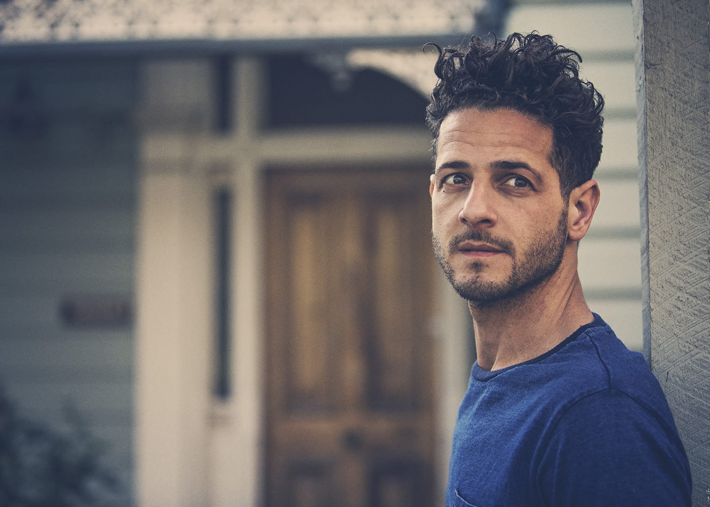 Lior (Finding Our Voice Performer) in front of a house in a blue shirt looking past the camera