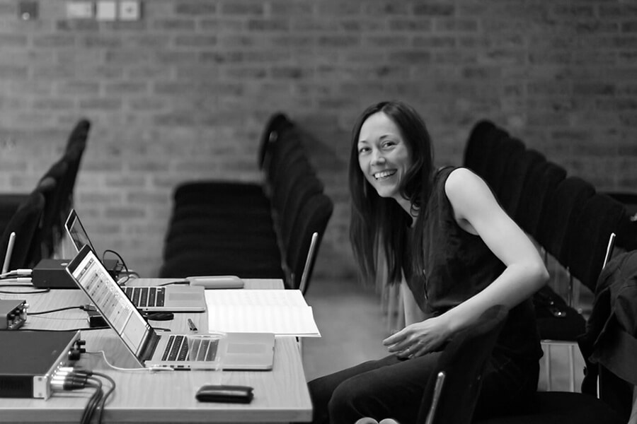 black and white image of musician Lisa Illean smiling at her desk while working on a composition