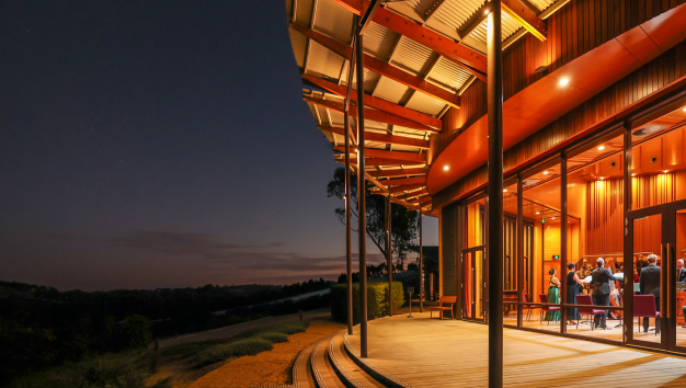 Exterior of the Ukaria Cultural centre at night from the side showing steps into the garden and bright orange light coming from inside