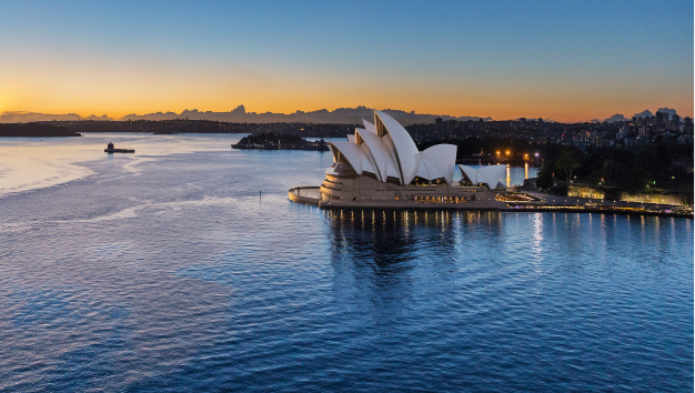 Exterior drone view of the Sydney Opera House at sunset on a clear blue sky day with a bright yellow horizon