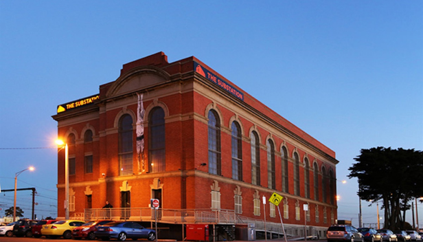 Exterior of Newport Substation at dusk with a blue sky background and lights illuminating the red brick